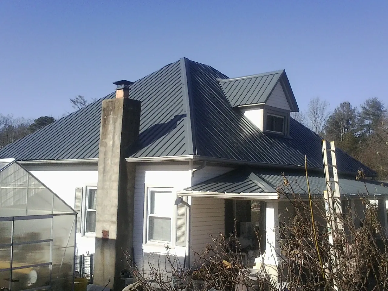 Dark blue standing seam metal roof on a white farmhouse with dormer — Slate & Tile Roof Repair by Roofing Brothers in Thomasville