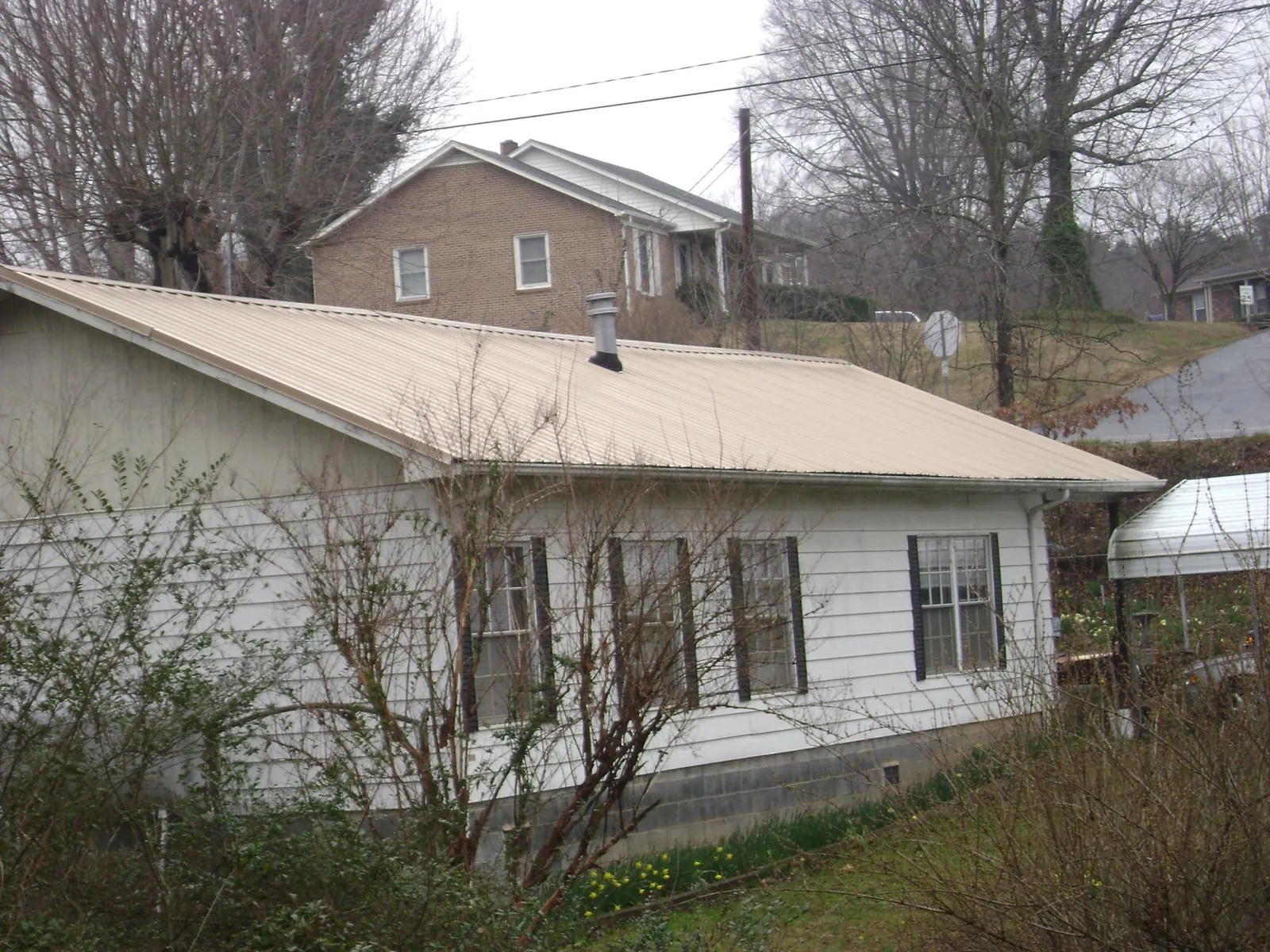 Tan metal roof on a white sided house set into a hillside — Commercial Roofing by Roofing Brothers in Thomasville